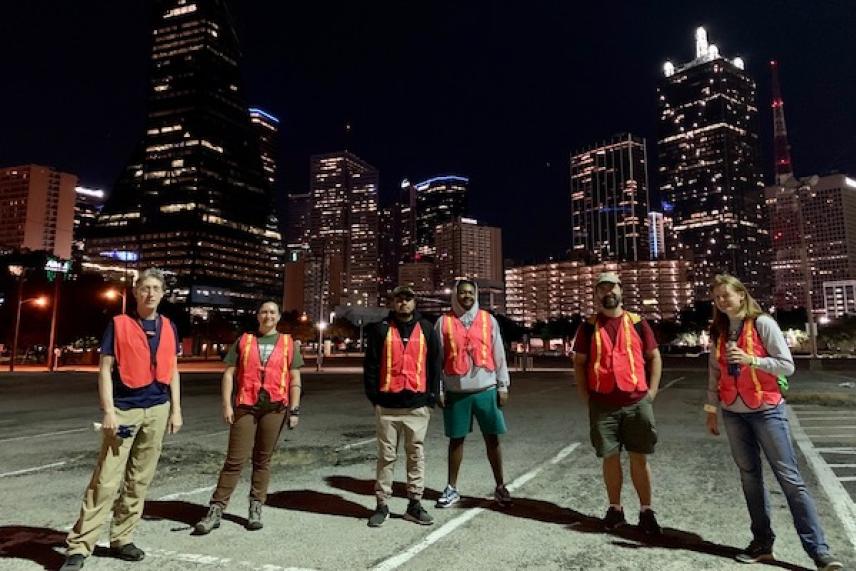 Group wearing safety vests in front of city skyline at night.