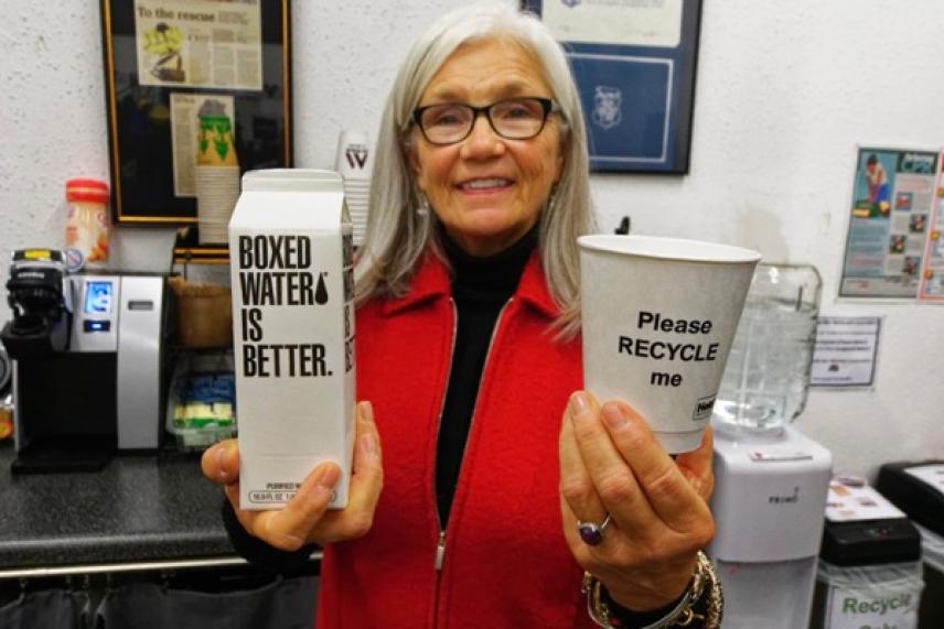 Woman smiling, holding a boxed water and a recyclable cup.
