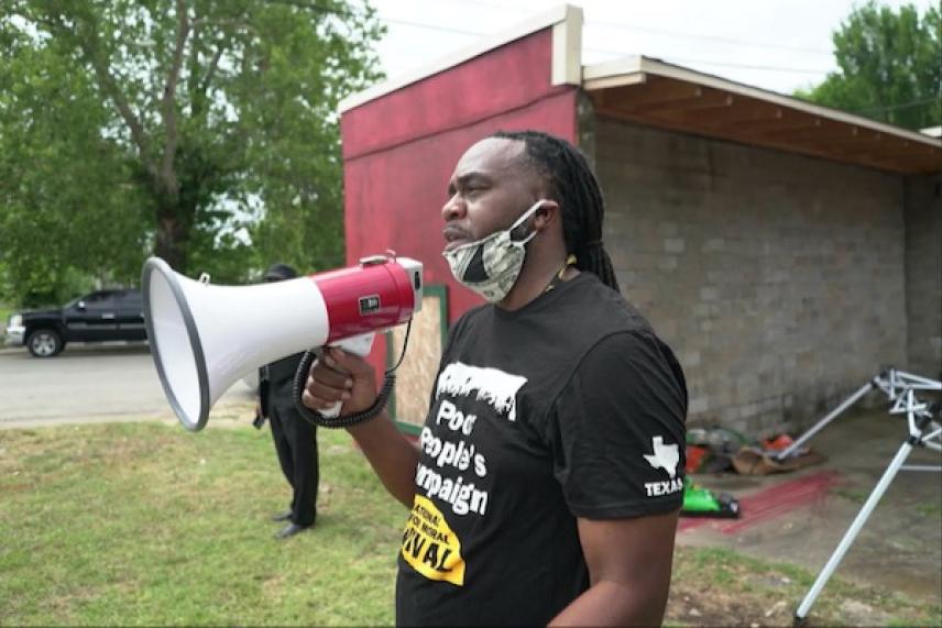 Man with megaphone wearing a mask stands outside, speaking.