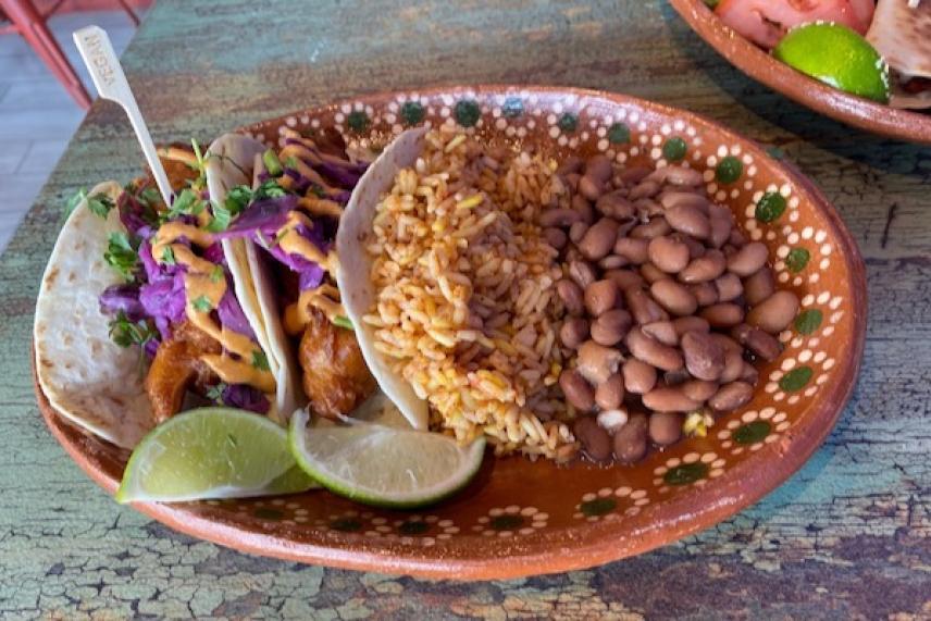 Tacos, rice, and beans with lime wedges on a decorated plate.
