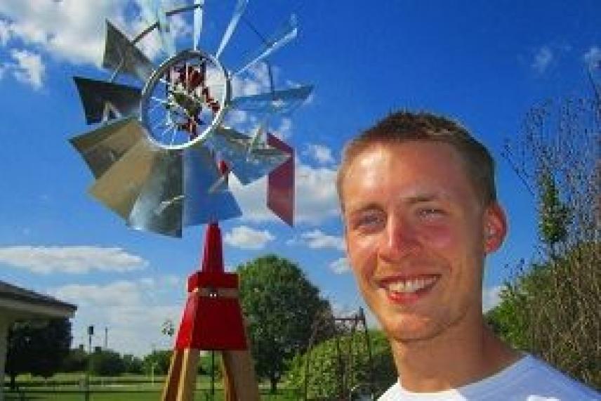 Smiling person in front of a windmill under a blue sky.