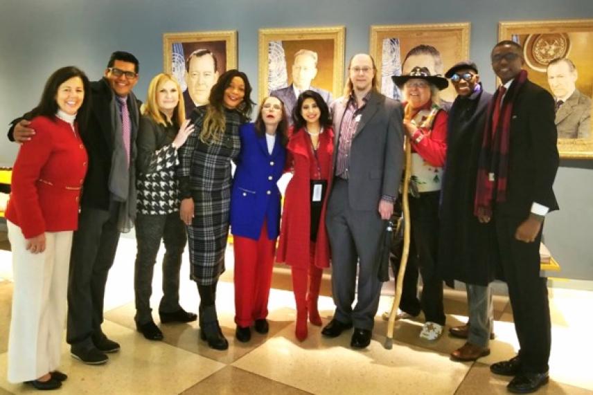A group of smiling people standing together indoors, with framed portraits on the wall behind them.
