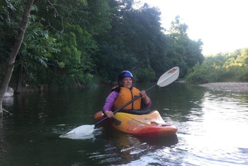 Kayaker paddles on a calm river, surrounded by lush greenery.