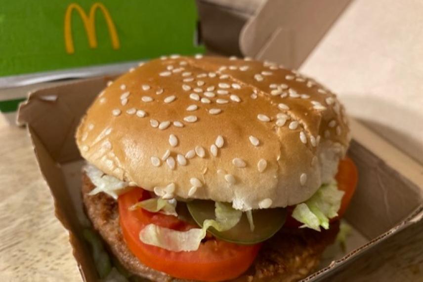 Sesame seed burger with lettuce, tomato, and pickles in a cardboard box.