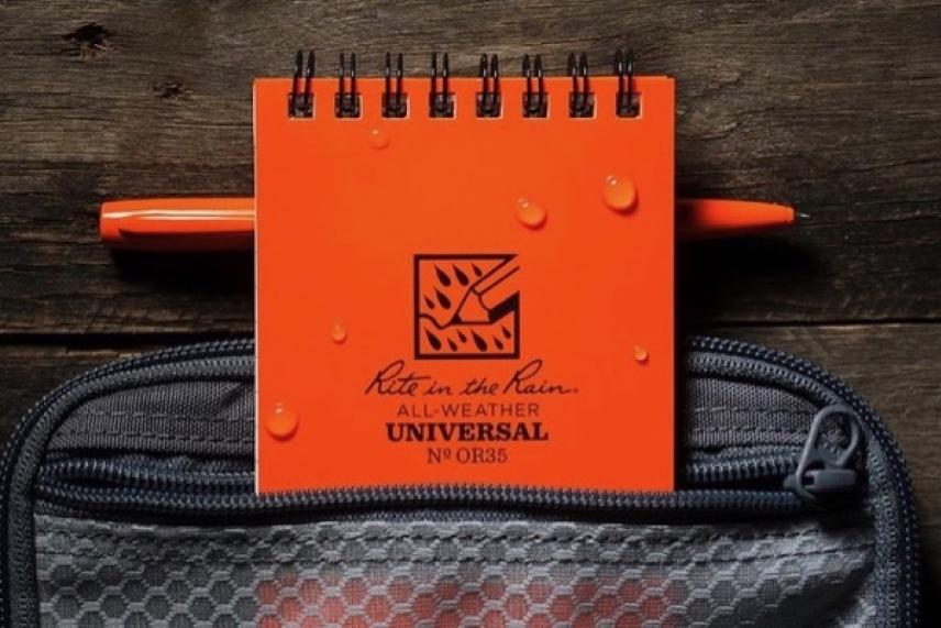 Orange notebook with raindrops next to a pen, resting on a zippered bag.