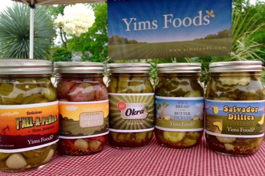 Five jars of pickled foods on a red gingham tablecloth.