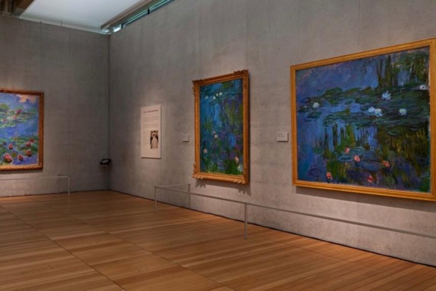Paintings in an art gallery with wooden floors and gray walls.