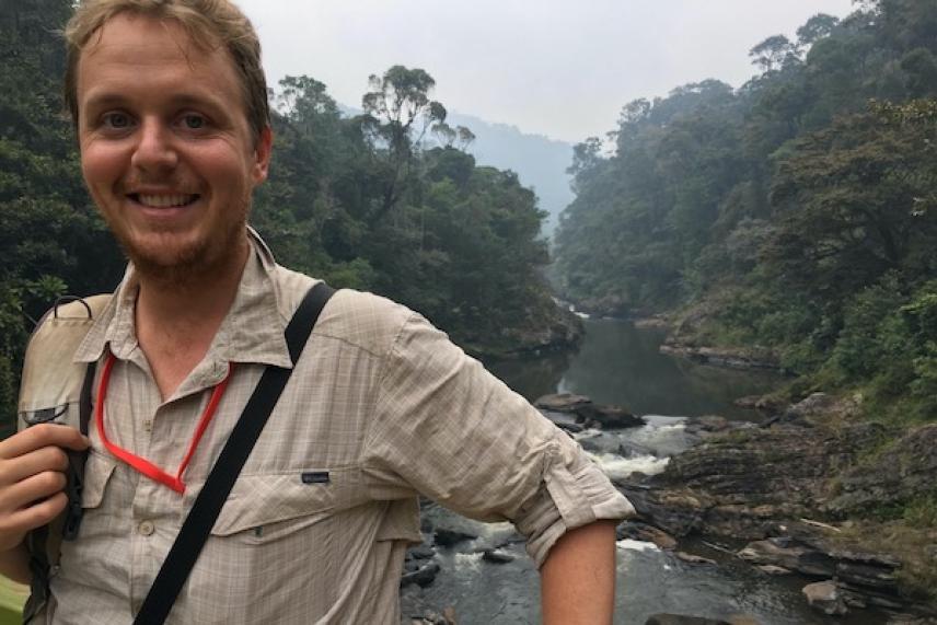 Smiling person in front of a forested river.