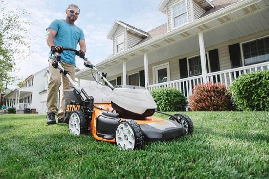 Man mowing lawn with an orange and white mower in front of a suburban house.