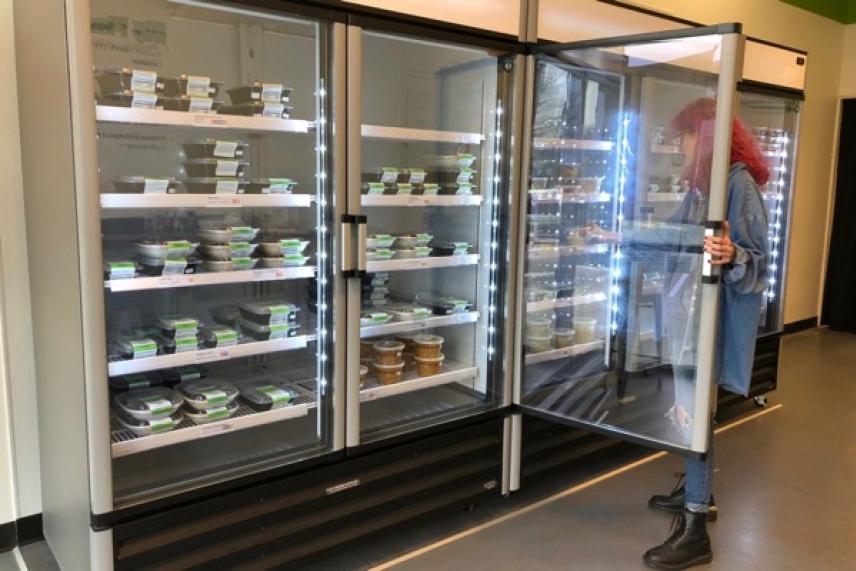 Person selecting meals from a large refrigerated display in a store.
