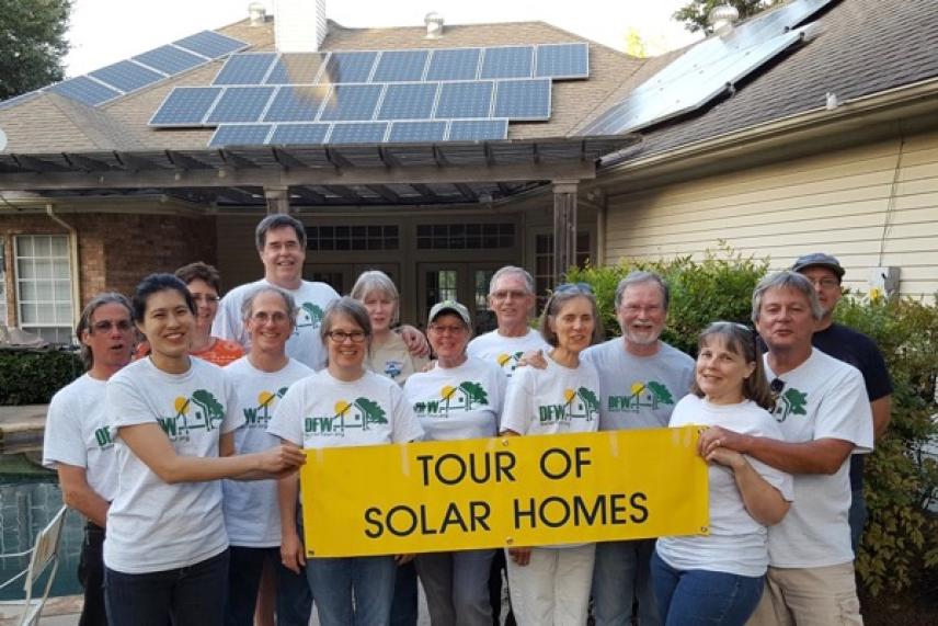 Group holding a "Tour of Solar Homes" banner in front of a house with solar panels.