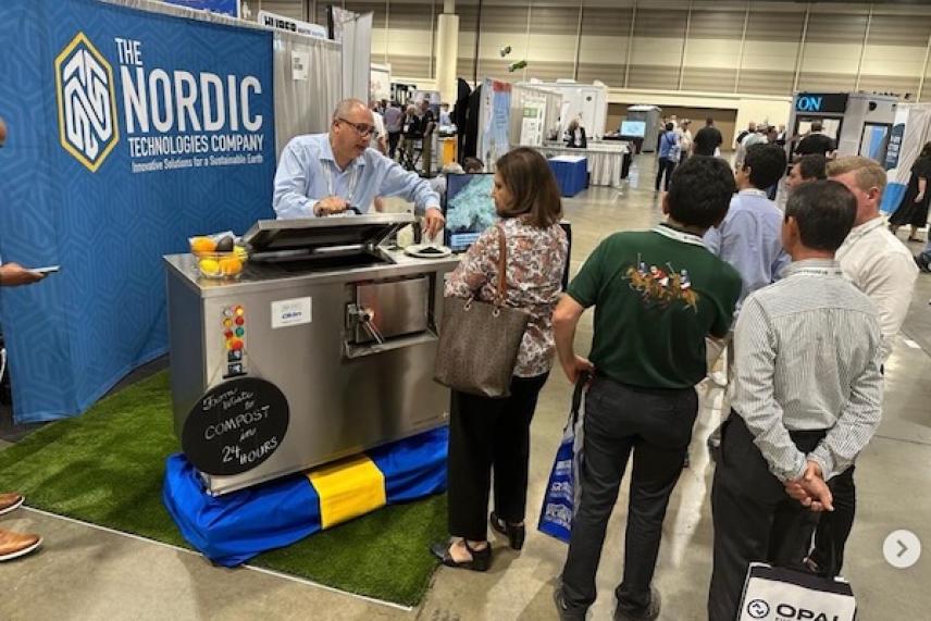 Man demonstrating equipment to a group at trade show booth.