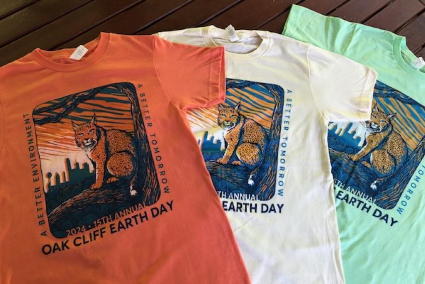Three Earth Day T-shirts in coral, white, and mint green with a graphic of a bobcat and city skyline.