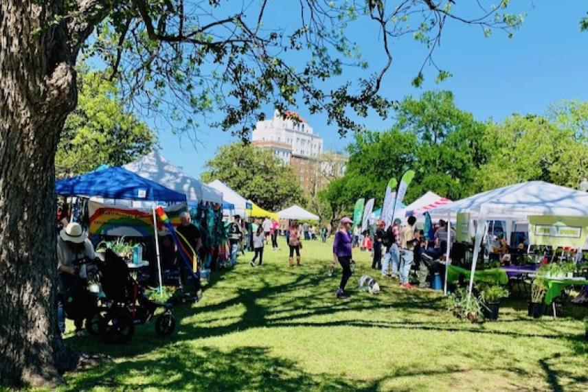 Outdoor market with tents, people, and trees under a clear blue sky.