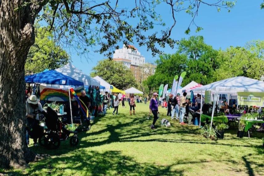 Festival in a park with tents, trees, and people under a clear blue sky.