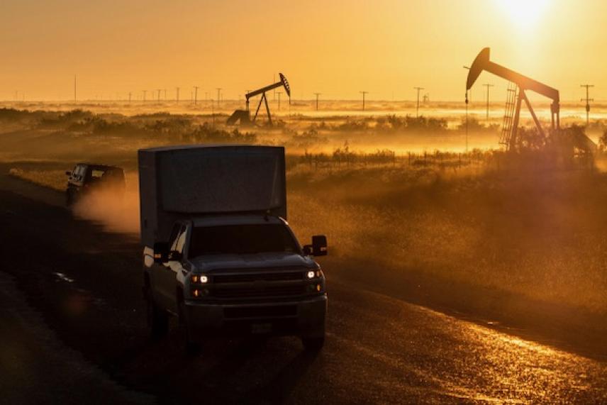 Truck driving on a rural road at sunrise, oil pumps in the background.