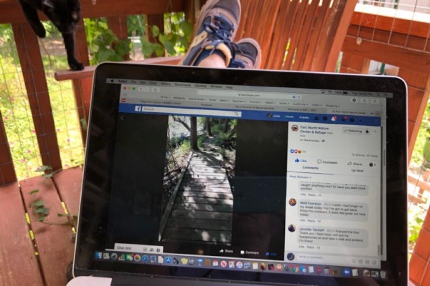 Laptop on lap, displaying a social media page, feet up on balcony railing.