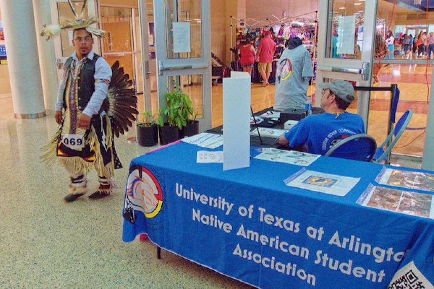 Native American student association booth, person in traditional attire nearby.