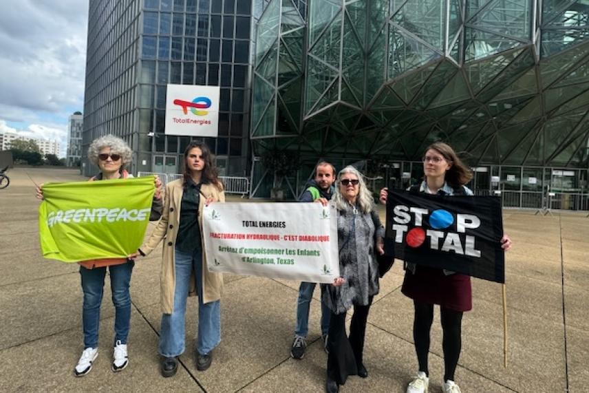 Protesters holding banners outside a modern glass building.