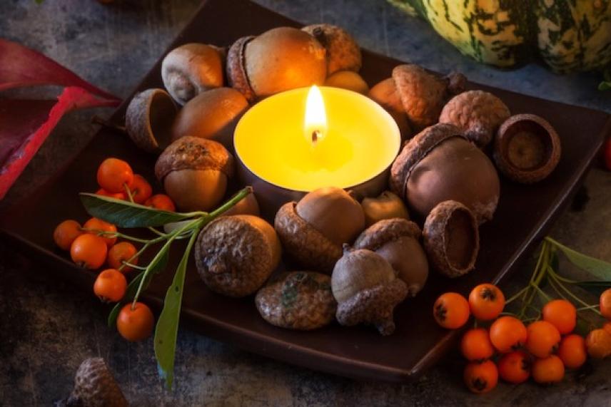 Candle surrounded by acorns and berries on a dark plate.