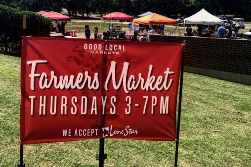 Red sign for a farmers market with tents in the background.