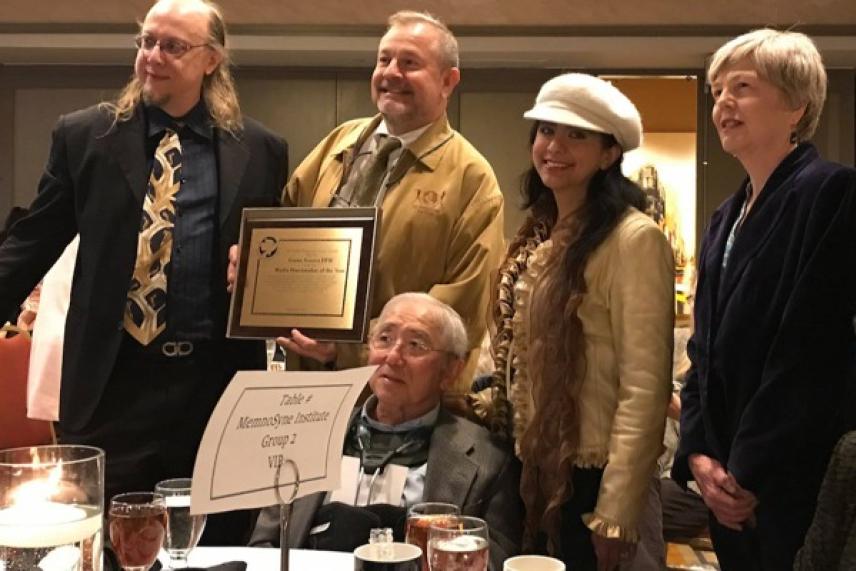 A group of smiling people at a banquet, one holding a framed award.