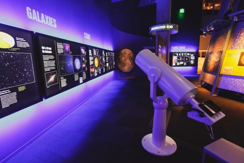 Interactive space exhibit with telescope, colorful displays, and celestial graphics.