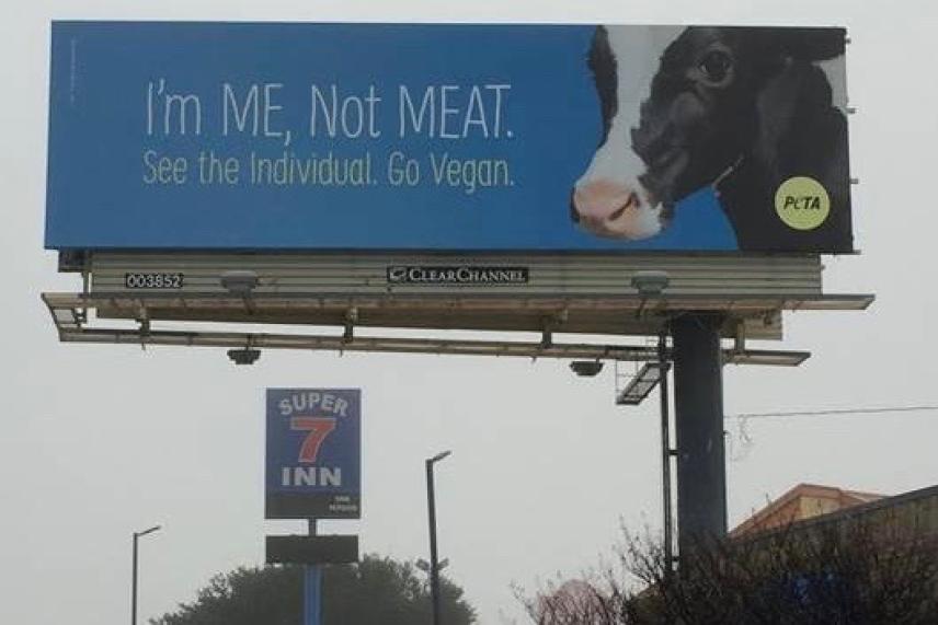 Billboard with a cow promoting veganism above a Super 7 Inn sign.