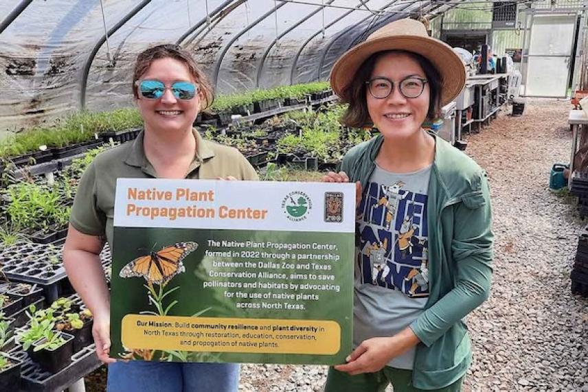 Two people in a greenhouse holding a Native Plant Propagation Center sign.