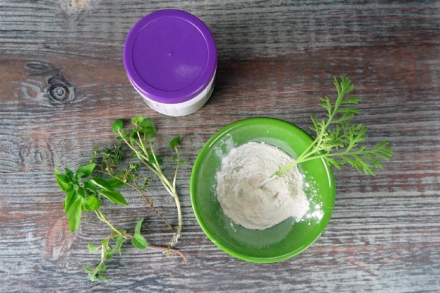 Green bowl of flour with herbs, purple-lidded container on wooden surface.