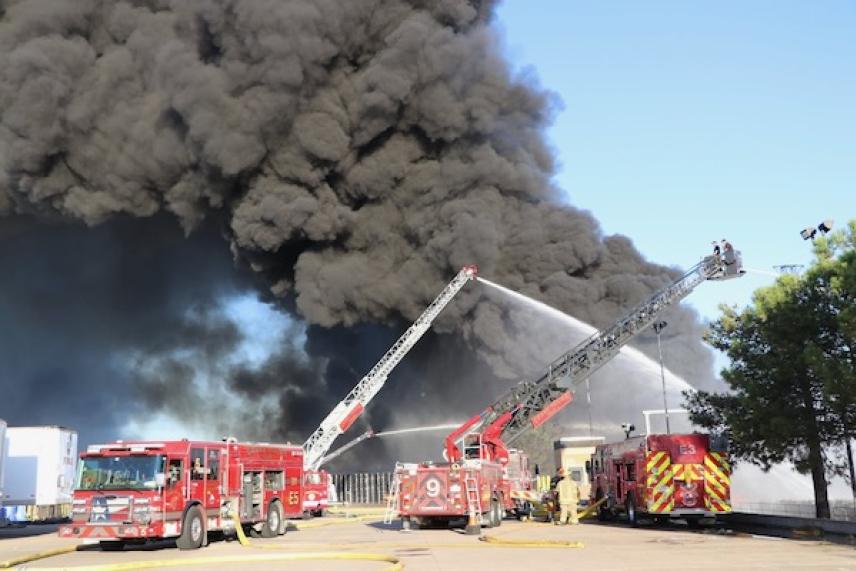 Firetrucks battling a large building fire with heavy black smoke.