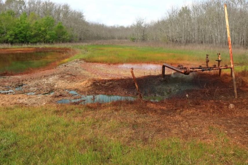 Abandoned rusty pipe structure in a grassy, marshy field.