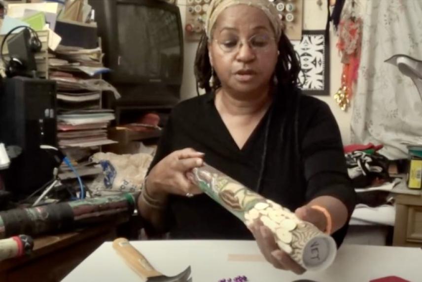 Woman holding a decorated cylindrical object in a cluttered room.