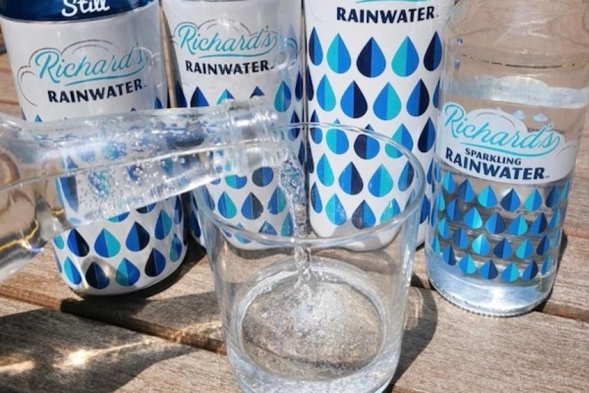 Cans and bottles of rainwater on a wooden table, pouring into a glass.