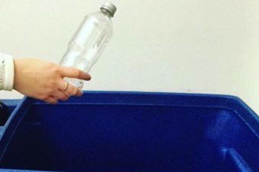 Hand holding a plastic bottle over a blue recycling bin.