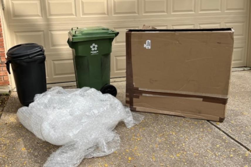 Trash bins, large cardboard box, and bubble wrap on driveway.