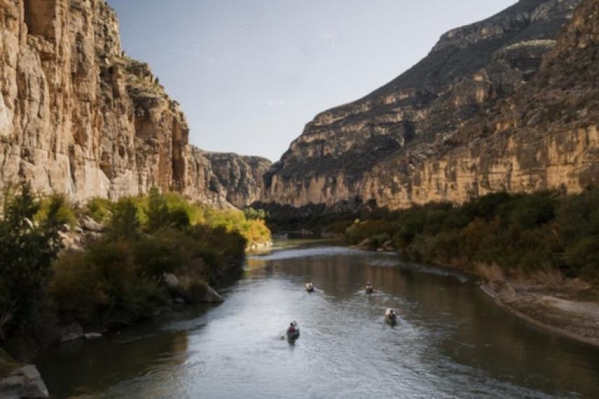 Canoes on a calm river between towering cliffs and green foliage.