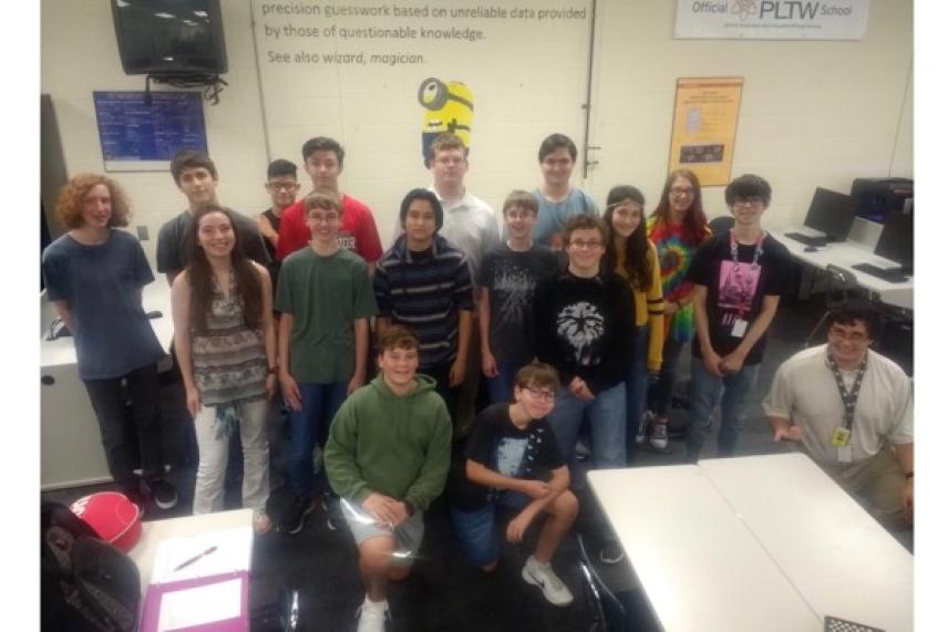 Class of students and a teacher posing in a tech classroom.