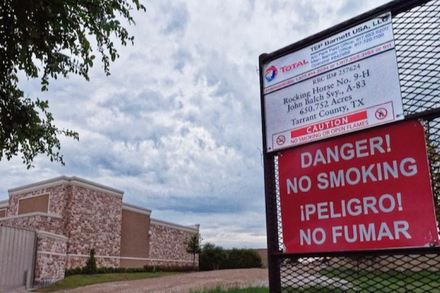 No smoking sign by a cloudy sky and industrial building.