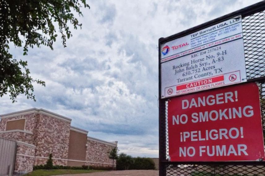 Red no smoking sign on a fence, cloudy sky, brown building nearby.