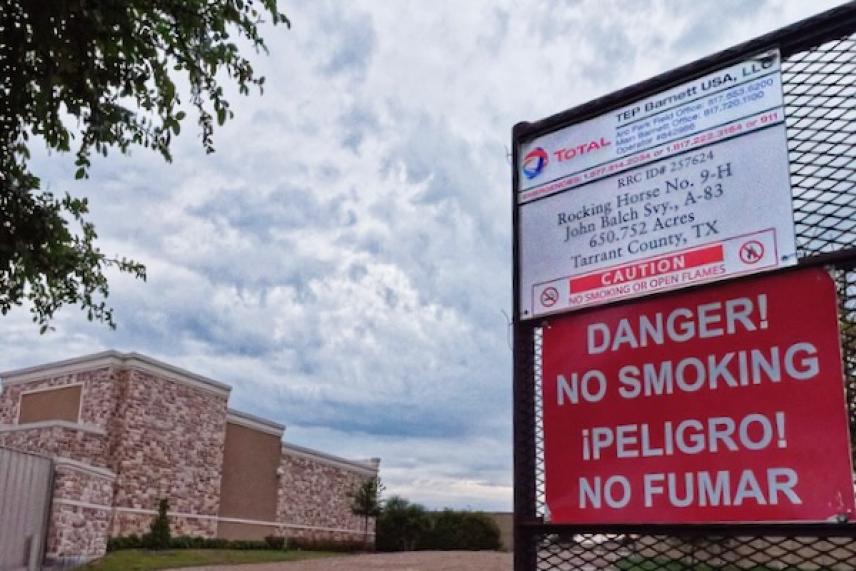 Red "No Smoking" sign on wire fence, cloudy sky background.