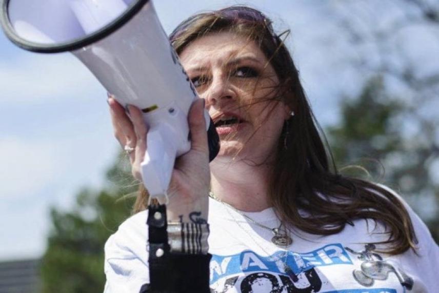 Woman speaks into a megaphone outdoors, wearing a white shirt.