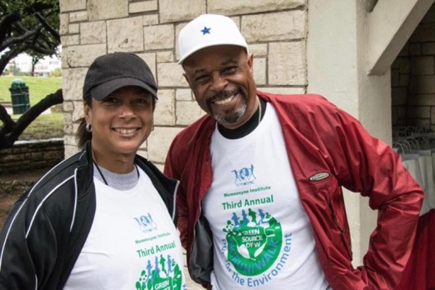Two smiling people outdoors in matching event shirts and hats.
