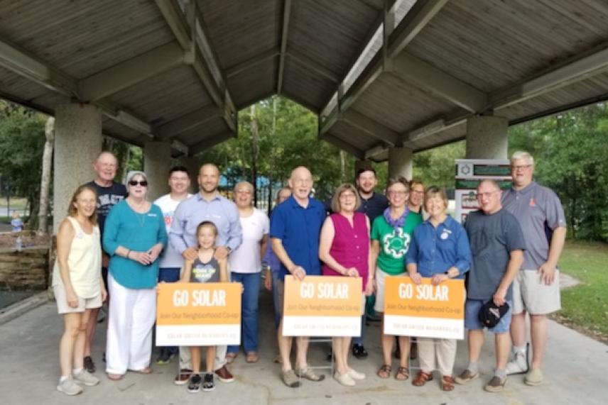 Group of people holding "Go Solar" signs under a pavilion.