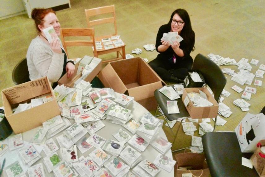 Two women sit on the floor, surrounded by several open boxes and stacks of letters.