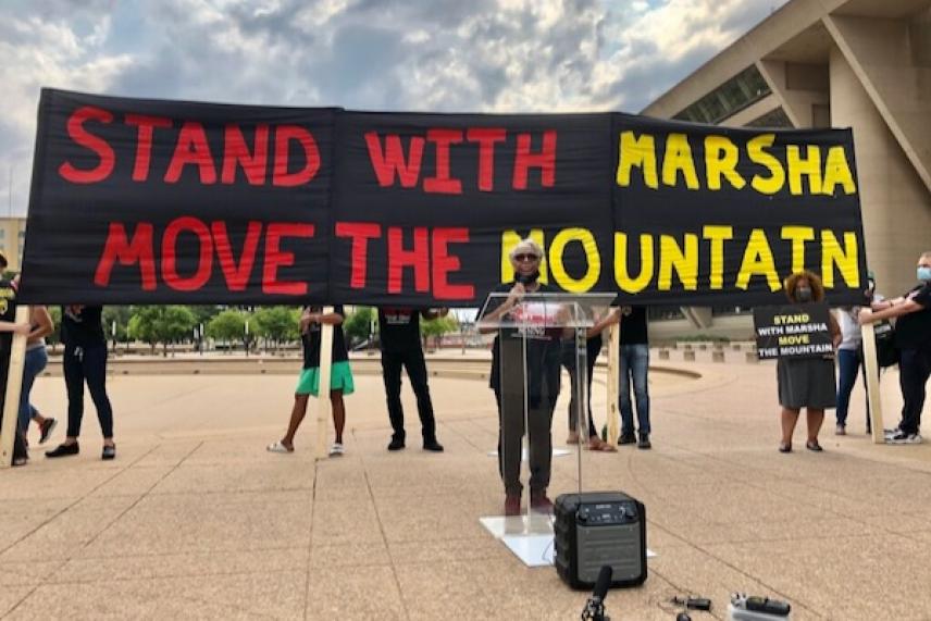 Protesters holding a large banner outdoors on a cloudy day.