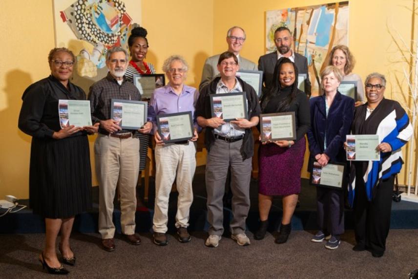 Group of diverse people smiling, holding certificates in a room with colorful art on the walls.
