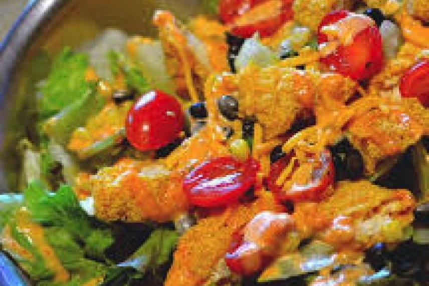 Colorful salad with lettuce, tomatoes, cheese, and orange dressing.