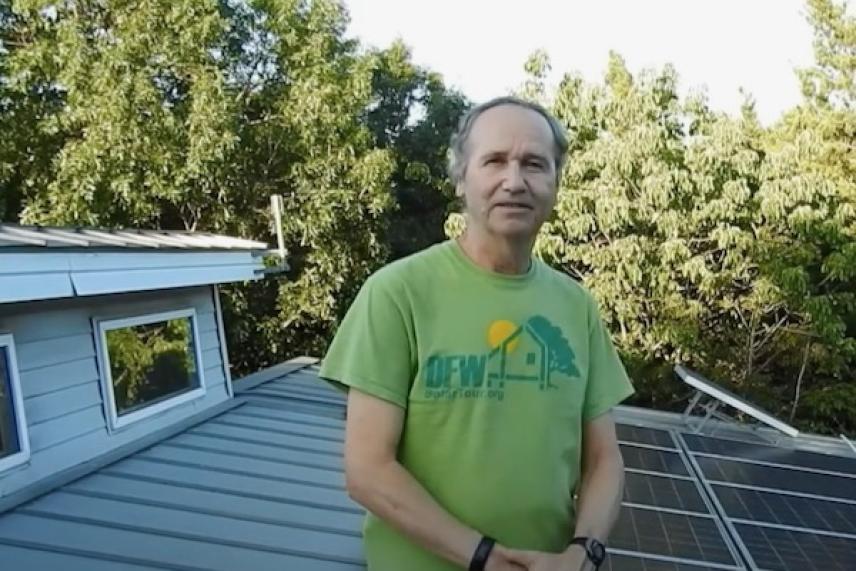 Man standing on a rooftop with solar panels and trees in the background.