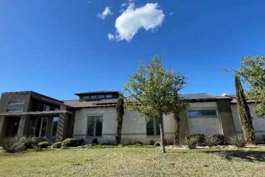 Modern house with a flat roof, trees, and a single cloud in a blue sky.